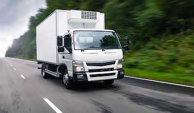 Ein weißer LKW fährt auf einer Straße. Durch die Bewegungsunschärfe ist die Straße und der Wald im Hintergrund nur unscharf zu erkennen.