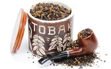 Eine mit Tabak gefüllte Pfeife lehnt an einer geöffneten Tabakdose mit der Aufschrift „TOBAK“. Auf dem strahlend weißen Untergrund liegt verteilt loser Tabak.